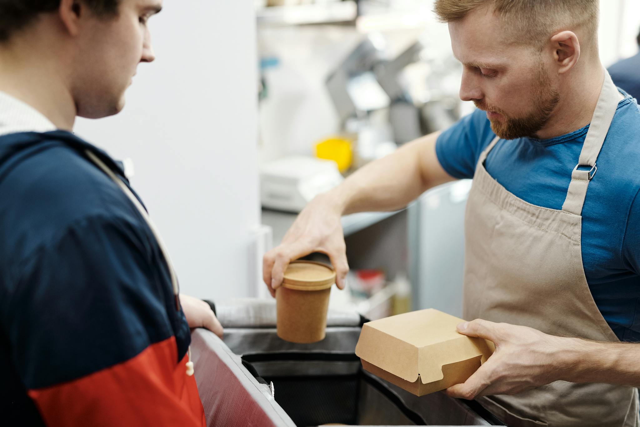 A server hands a paper container and cup to a customer, exemplifying modern takeaway service.