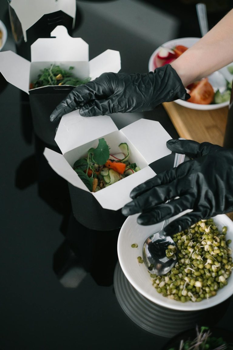 Gloved hands preparing fresh salad takeout in eco-friendly containers for delivery.
